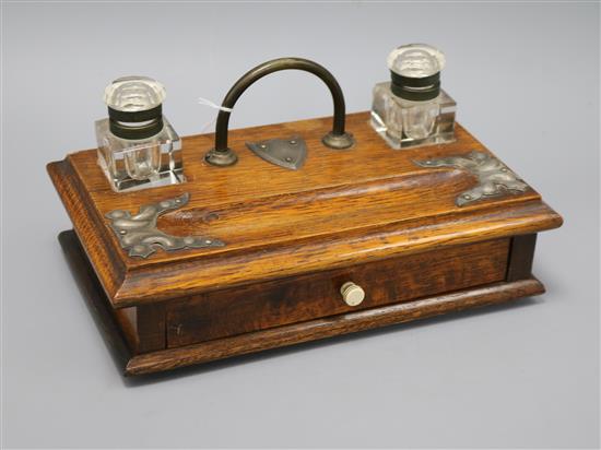 An oak desk stand with silver-plated mounts, fitted two plain inkwells, pen tray and drawer with ivorine handle length 29cm